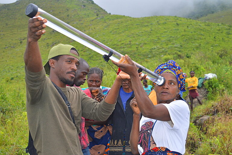 In Angola, project coordinator Mona Bunga instructs biodiversity monitor Teresa Sakata on how to use a turbidity tube to measure water quality in a stream flowing out of a restored patch of Afromontane Forest. Image by Ryan Truscott for Mongabay.